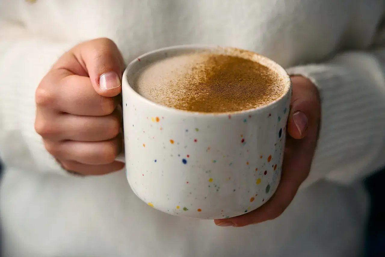 Ciepły napój w kolorowym kubku, posypany cynamonem. Czy to chai latte? Idealny na chłodne dni.