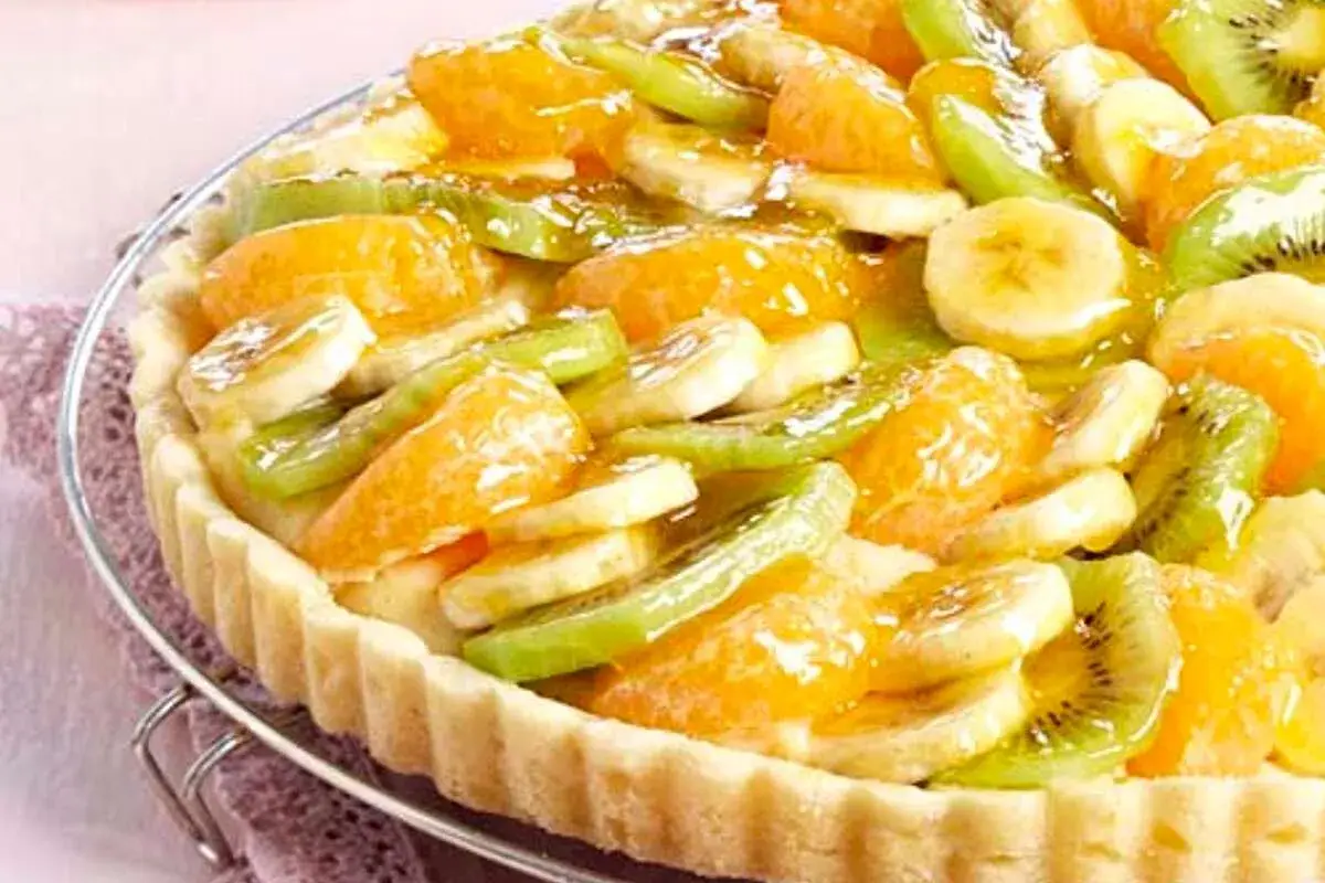 Tarte aux fruits frais sur une base de crème pâtissière. Des rondelles de banane, de kiwi et des quartiers d'orange sont disposés sur le fond de tarte.