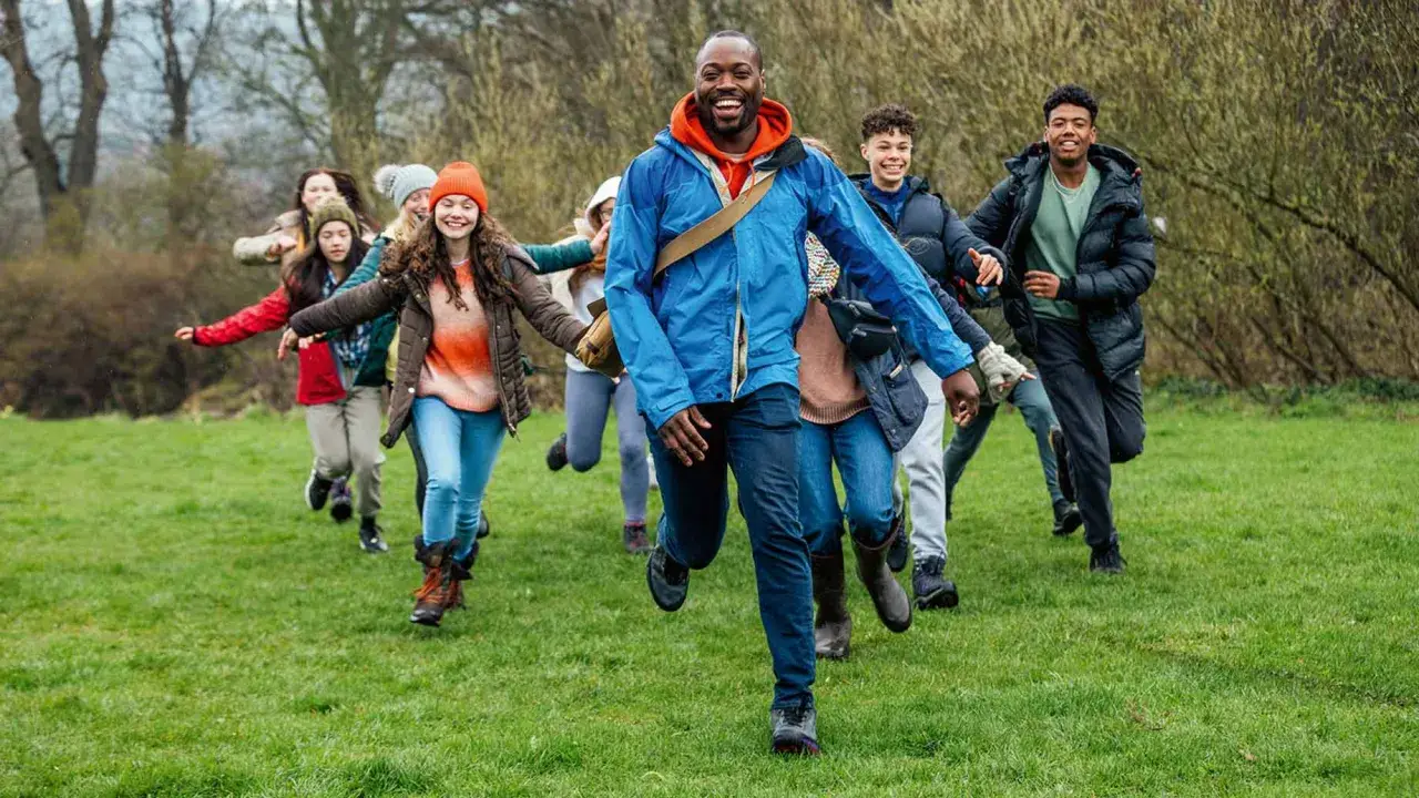 Lehrer und Schüler rennen lachend über eine grüne Wiese. Perfekt, um eine Klassenfahrt zu organisieren und Abenteuer zu erleben!