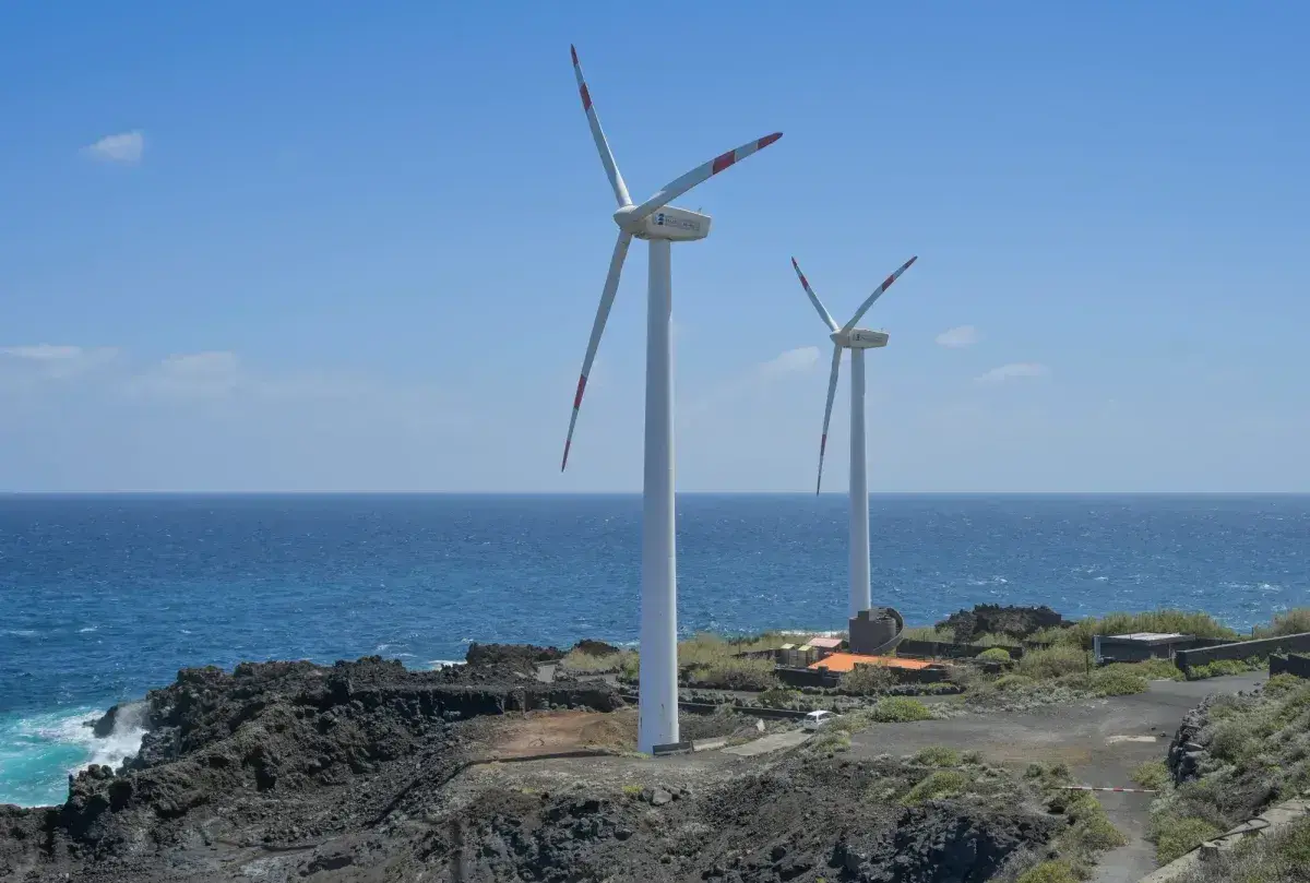 Zwei Windräder stehen an einer felsigen Küste Spaniens. Sie sind Teil des Strommixes und erzeugen saubere Energie.