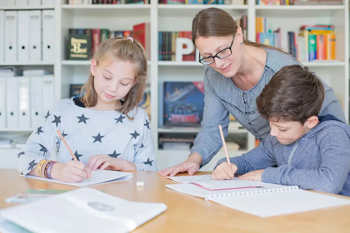 Lehrerin hilft zwei Schülern bei der Nachhilfe Realschule. Sie schreiben konzentriert in ihre Hefte.