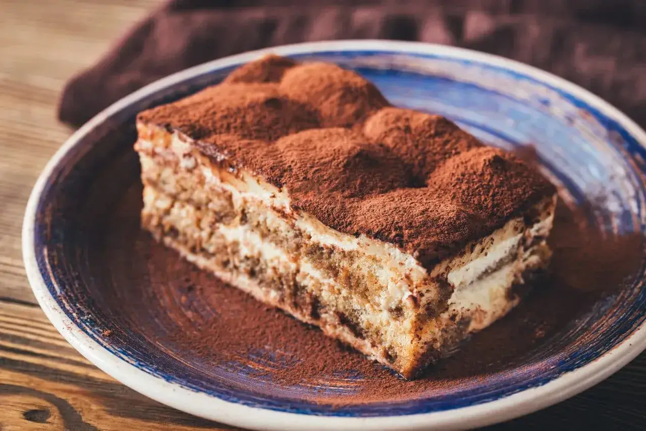 Pyszny kawałek tiramisu z mascarpone, posypany kakao, na talerzu. Idealny sprawdzony przepis na deser.