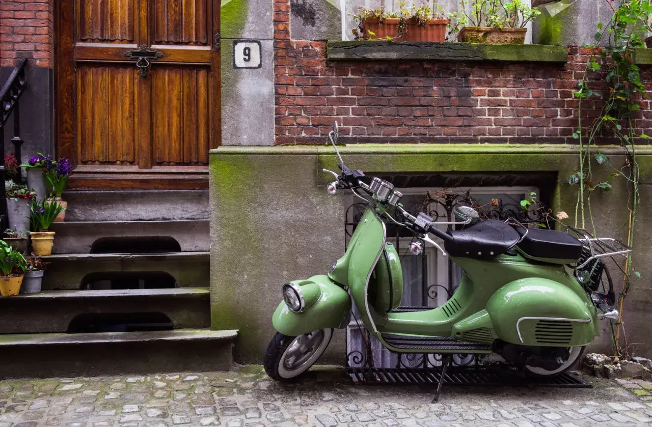 Zielony skuter, klasyk, czeka na właściciela. Parkowanie motocykla na chodniku przed drzwiami z numerem 9.