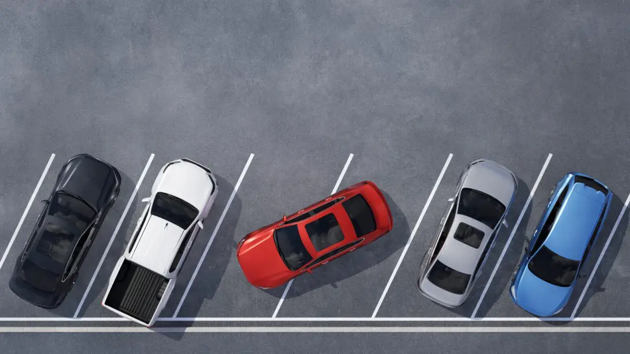 Czerwony samochód zajmuje dwa miejsca parkingowe, blokując sąsiednie pojazdy. Obok stoją czarny, biały pickup, srebrny i niebieski.