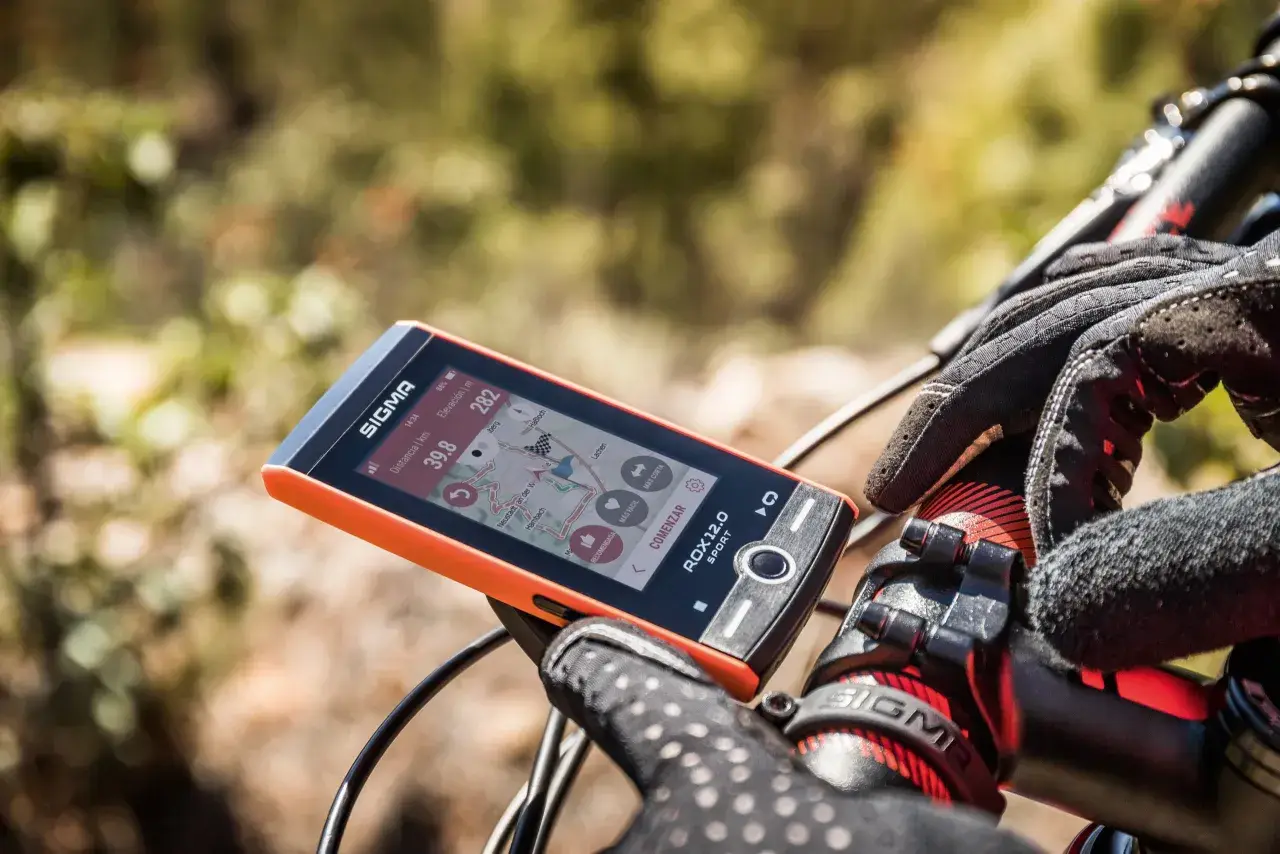 Pomarańczowy licznik rowerowy Sigma ROX 12.0 Sport pokazuje dystans 39.8 km i wysokość 282 m. Rękawiczka rowerowa na kierownicy.