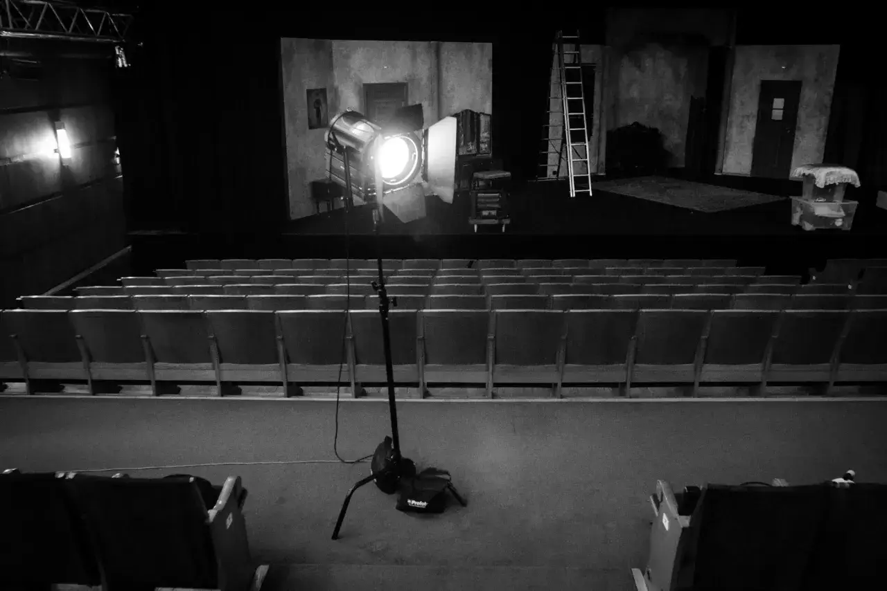 Teatr w czerni i bieli. Na scenie reflektor fresnel oświetla dekoracje, a przed nią puste rzędy siedzeń.