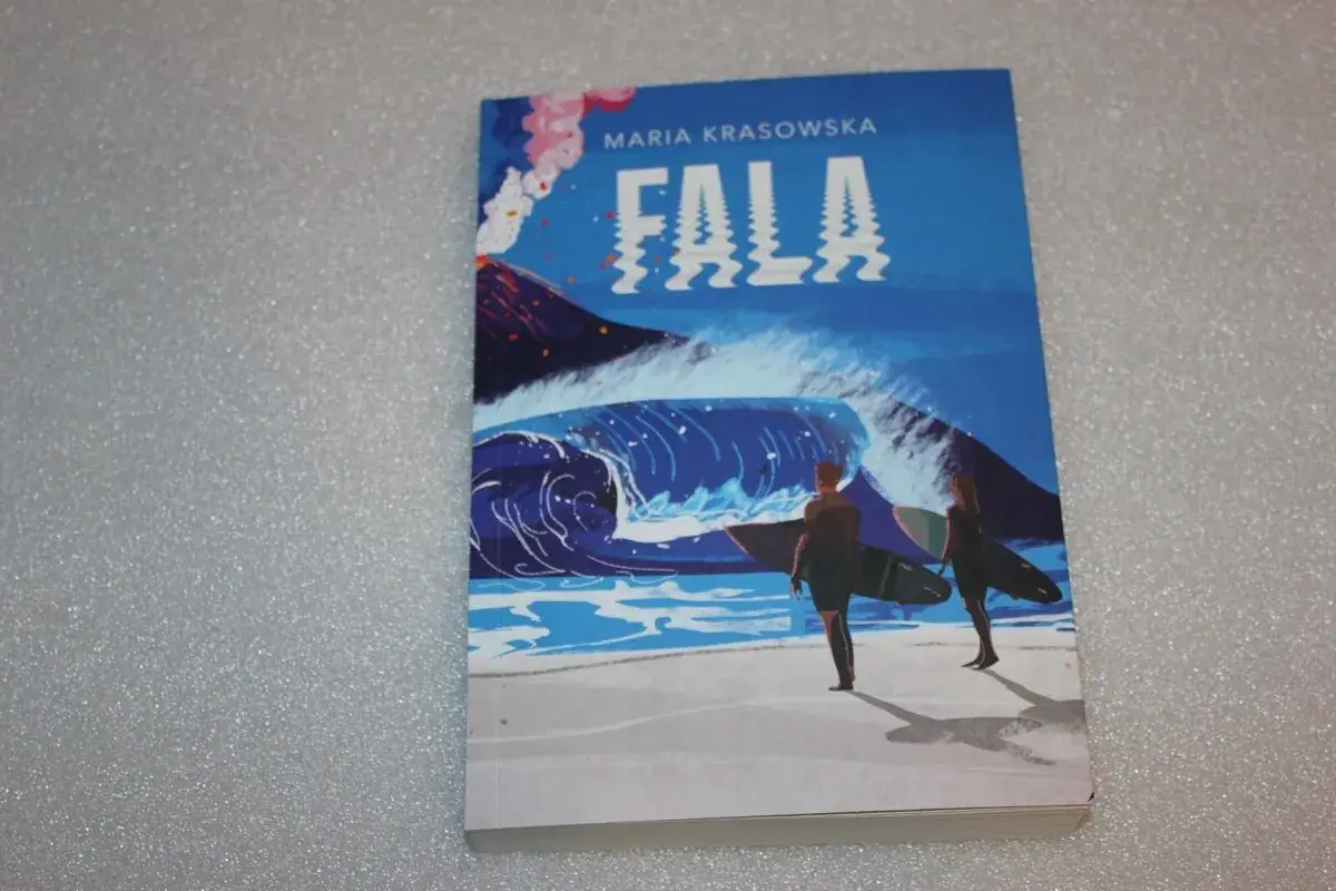 Okładka książki "Fala" Marii Krasowskiej. Dwie postacie z deskami surfingowymi stoją na plaży, patrząc na ogromną falę i wulkan.
