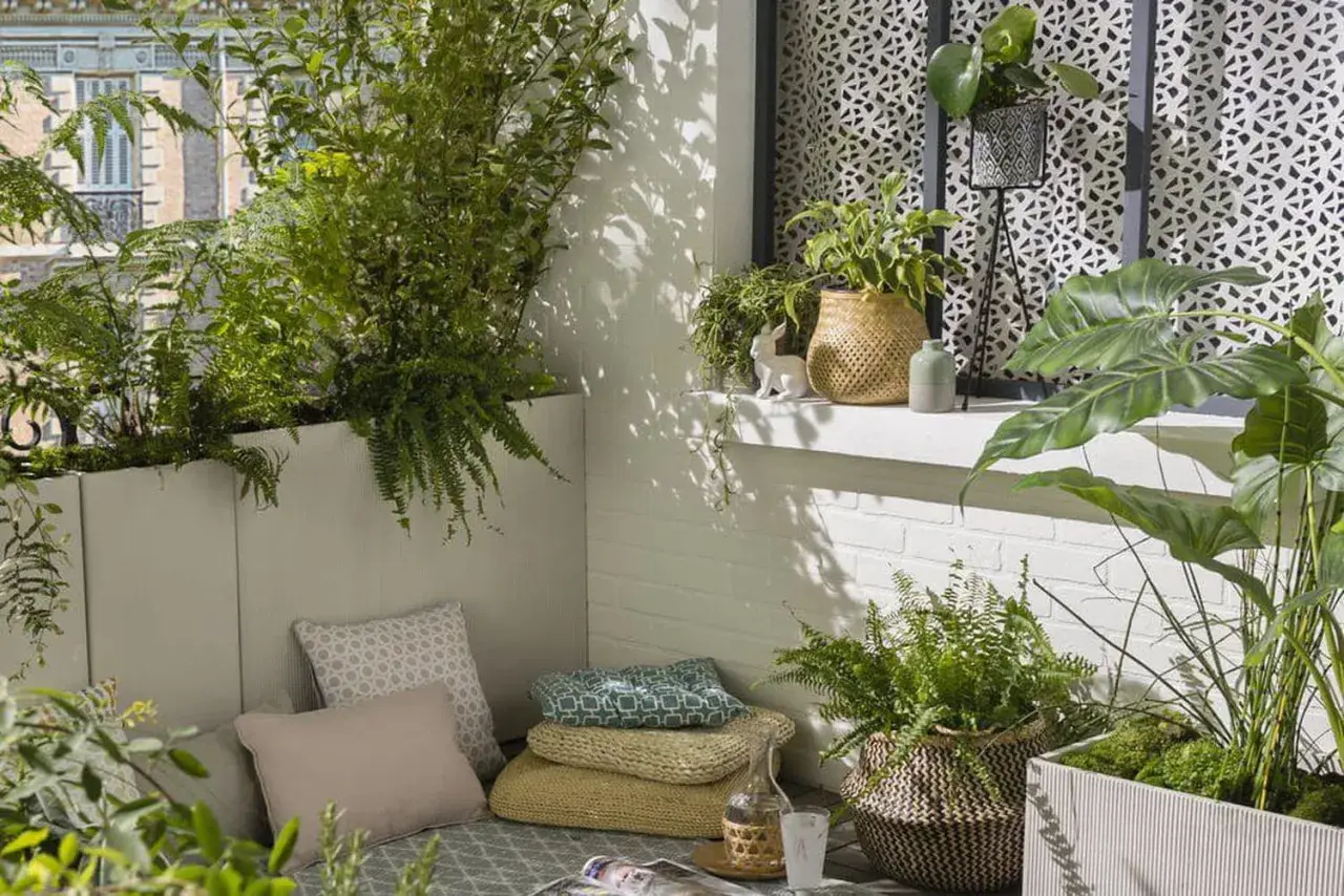 Un coin détente sur un balcon avec une plante brise-vue qui pousse vite en bac, des coussins et des plantes vertes.
