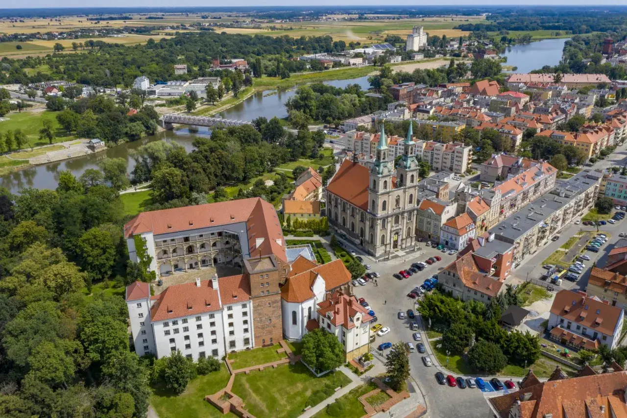 Zamek Piastów Śląskich w otoczeniu miasta i rzeki. Zabytkowa budowla z czerwonymi dachami, obok katedra z zielonymi wieżami.