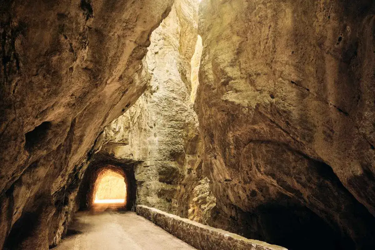 La strada della forra si snoda tra imponenti pareti rocciose, con un tunnel che si apre verso una luce accecante.