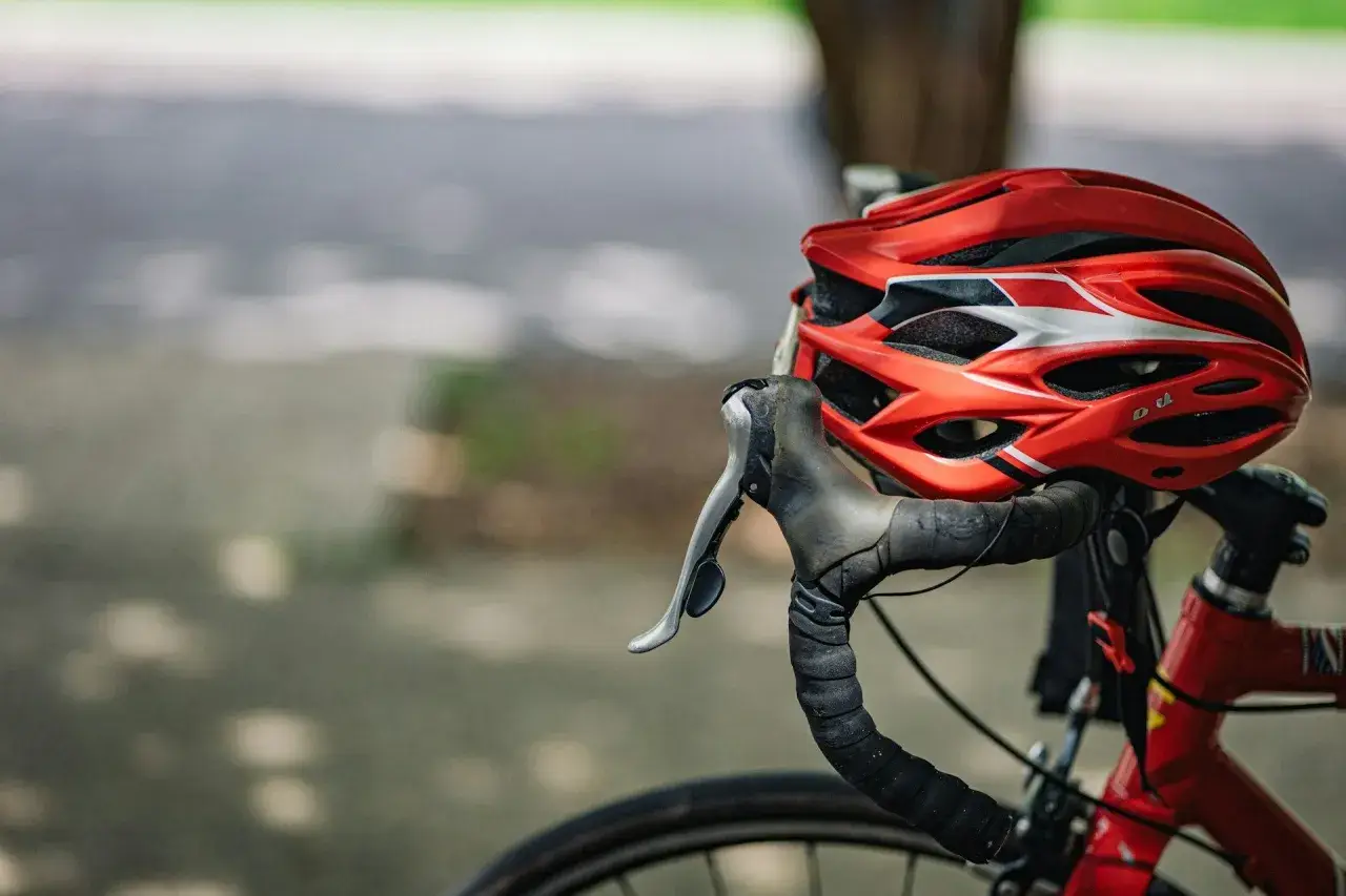 Czerwony kask rowerowy i kierownica z owijką. Niezbędne wyposażenie rowerzysty na bezpieczną podróż.
