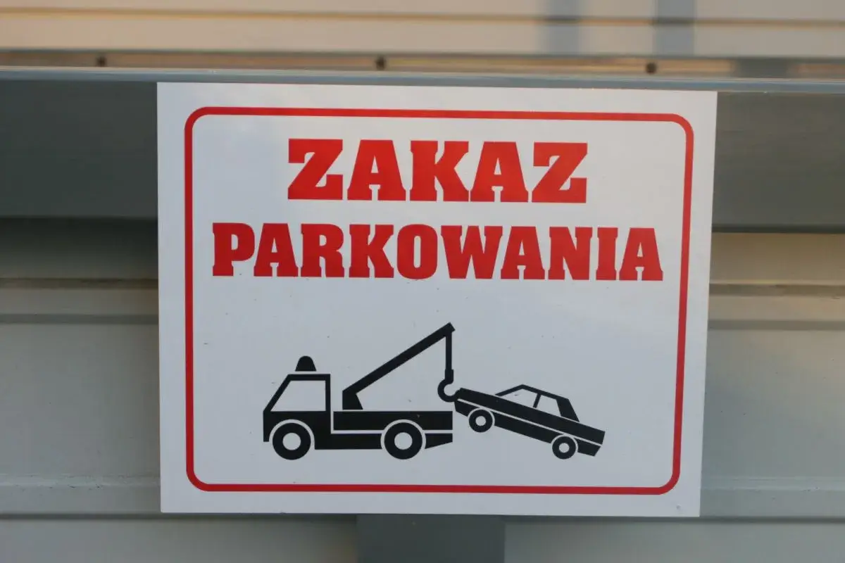 Zasady parkowania na parkingu: zakaz parkowania, holowanie pojazdów. Znak ostrzega przed odholowaniem źle zaparkowanego auta.