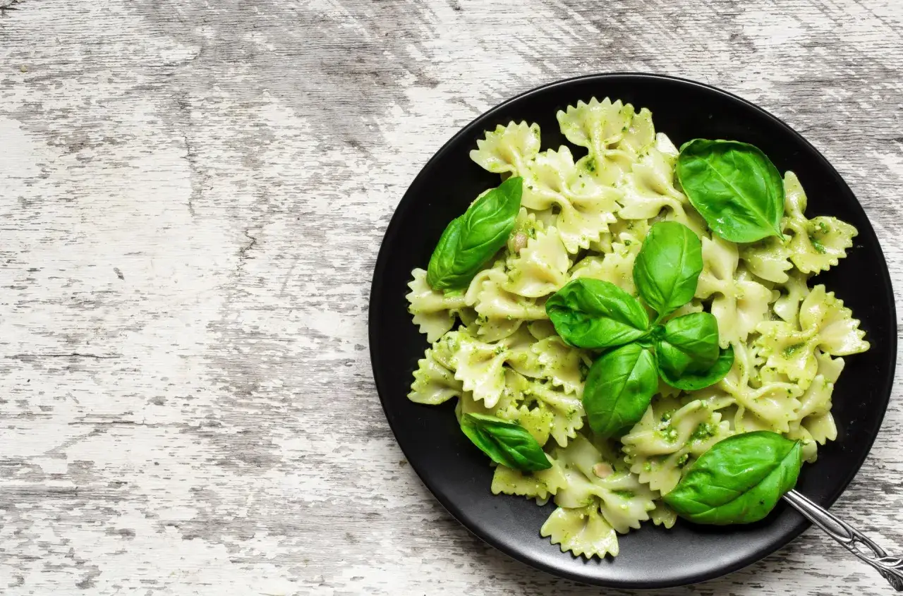 Lekkostrawny makaron farfalle z pesto i świeżą bazylią na czarnym talerzu, gotowy do podania.