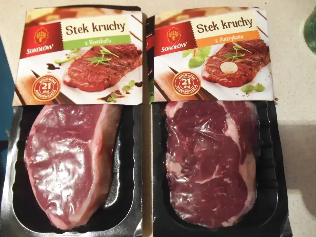 Dwa opakowania steka wołowego z widocznymi surowymi mięsami i zdjęciami gotowych steków.