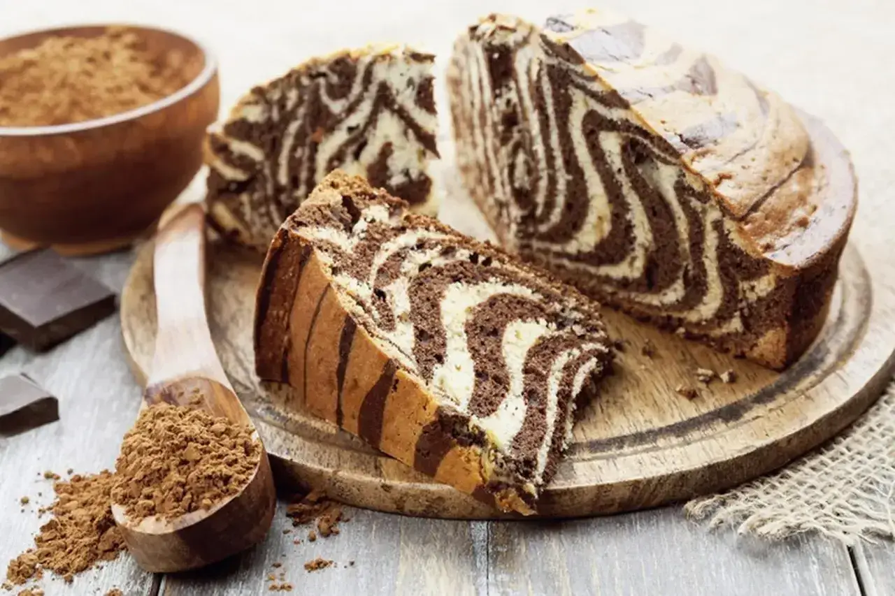 Wilgotne ciasto zebra z czekoladowymi i waniliowymi pasami, pokrojone na plastry, obok kakao i czekolady.