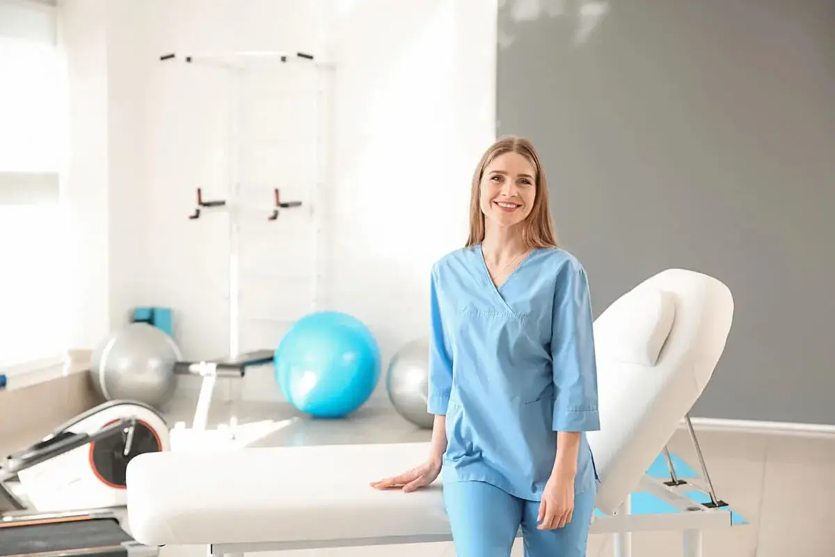 Uśmiechnięta fizjoterapeutka w gabinecie rehabilitacyjnym. Zastanawiasz się, ile zarabia fizjoterapeuta?