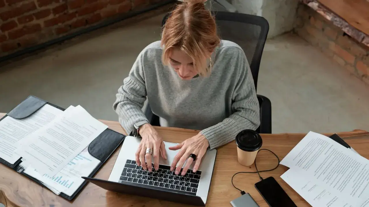 Kobieta pracuje przy laptopie, analizując dokumenty. Zastanawia się, czy umowa zlecenie wlicza się do stażu pracy, szukając odpowiedzi online.