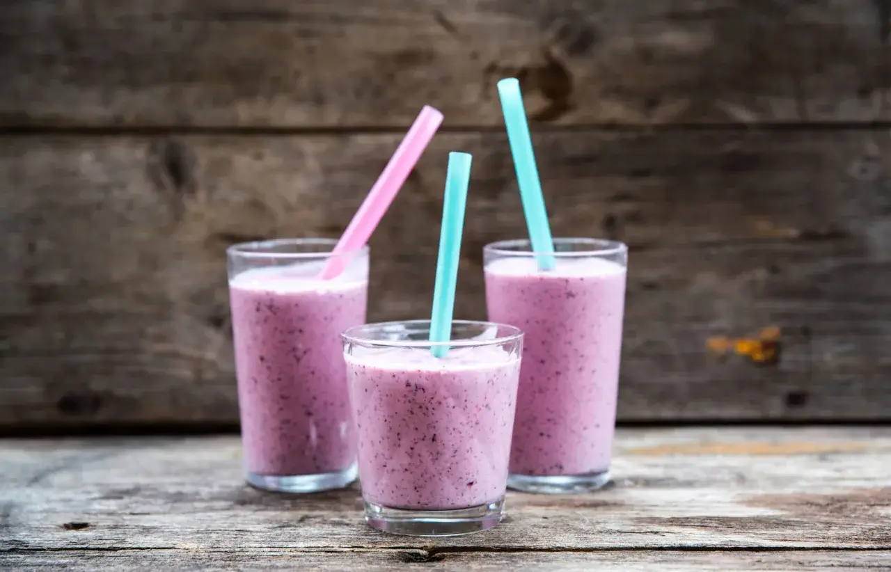 Tre glas med lila smoothie, perfekta för ett snabbt smoothie recept. Blå och rosa sugrör sticker upp.