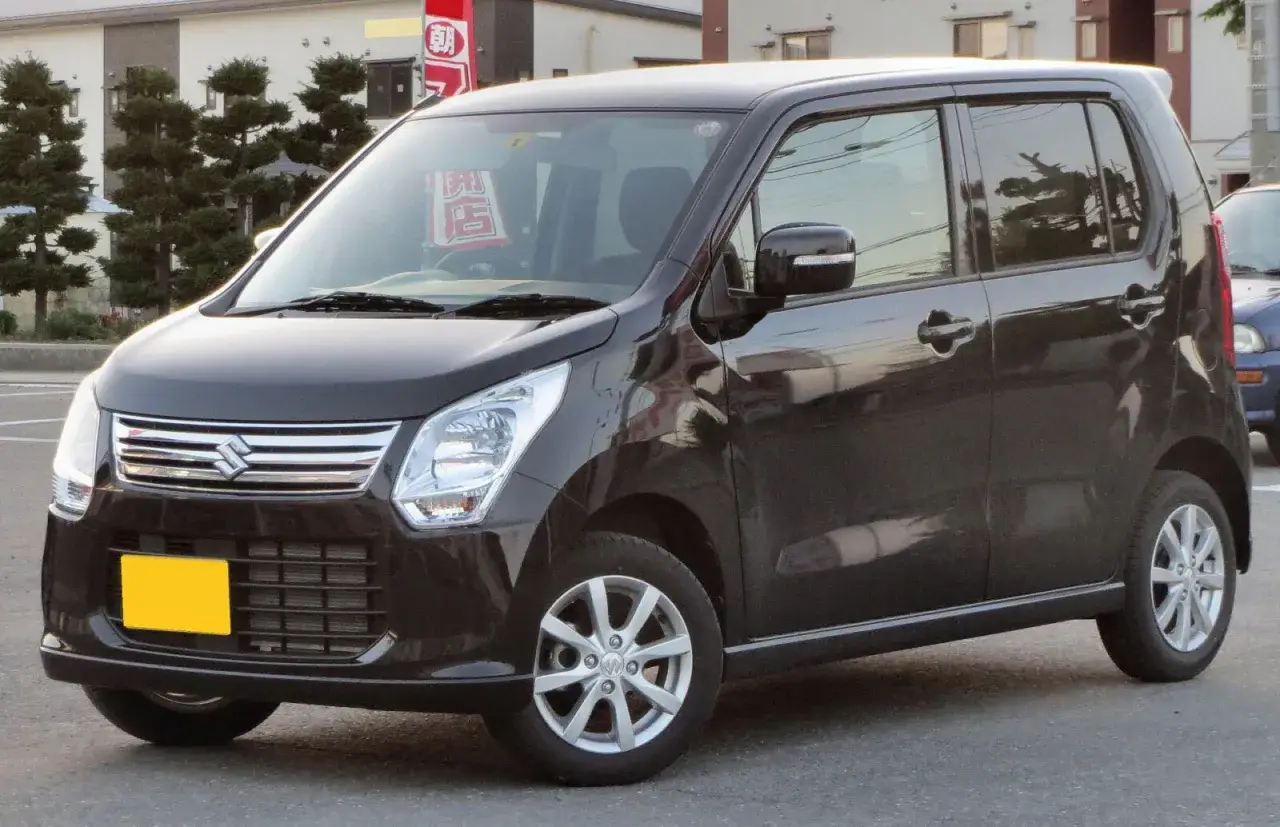 Ciemny Suzuki Wagon R+ z żółtą tablicą rejestracyjną, zaparkowany na ulicy.