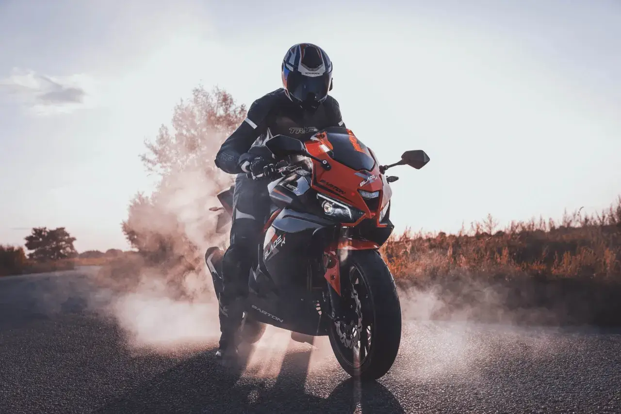 Motocyklista w kasku i kombinezonie na sportowym motocyklu, otoczony dymem. Czy motorem można jeździć po autostradzie? Tak, jeśli spełnia określone wymogi.