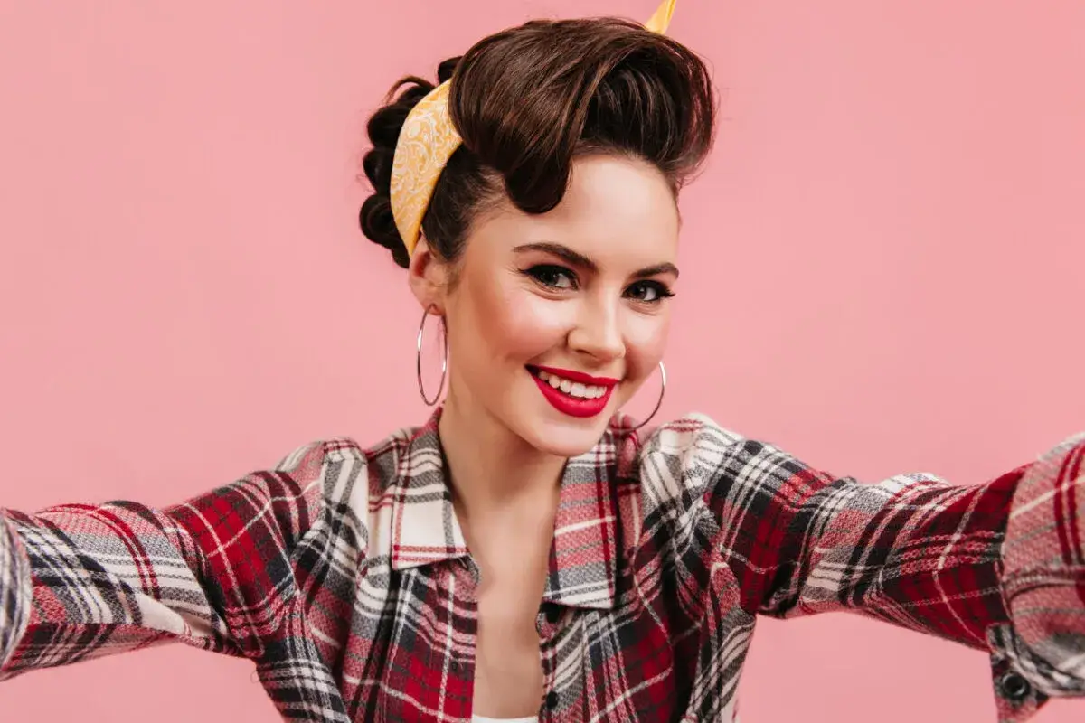 Uśmiechnięta dziewczyna w stylu pin up, z burzą brązowych włosów upiętych w kok i żółtą bandanką, w kraciastą koszulę.