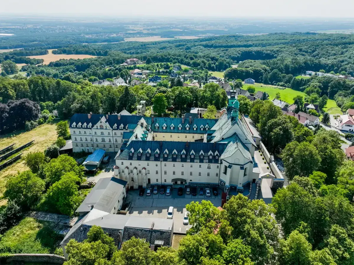 Widok z lotu ptaka na klasztor na Górze Świętej Anny. Rozległy kompleks budynków z zielonymi dachami otoczony bujną zielenią.