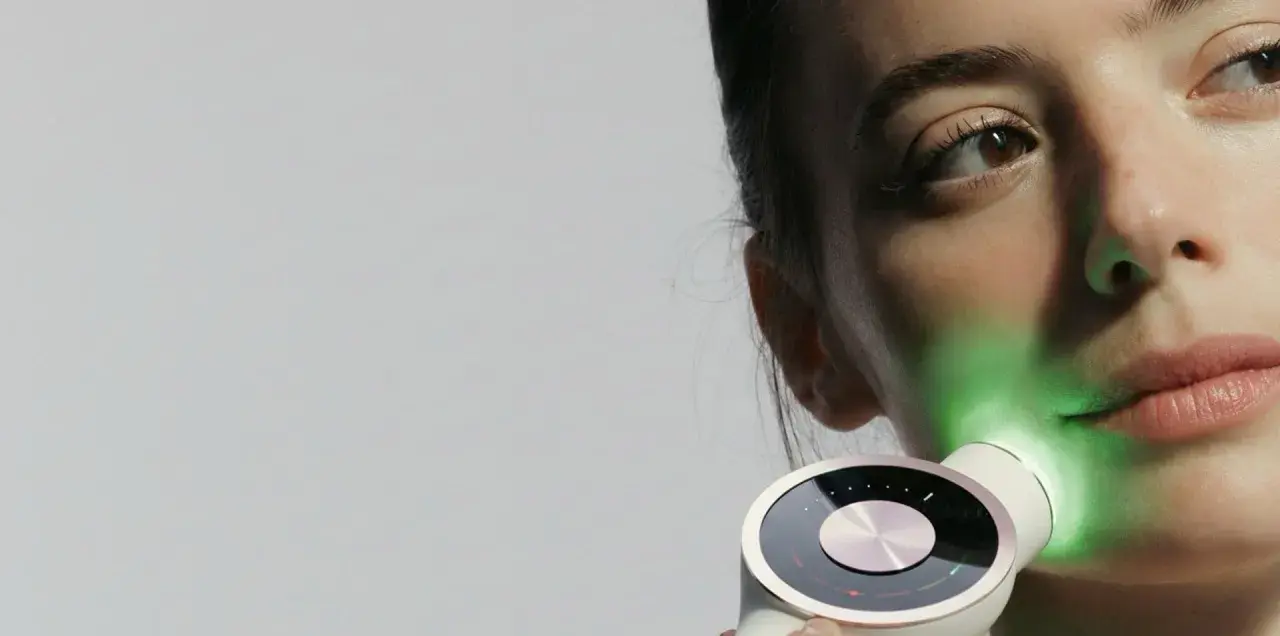Une femme utilise un appareil de luminothérapie LED pour le visage, projetant une lumière verte apaisante.