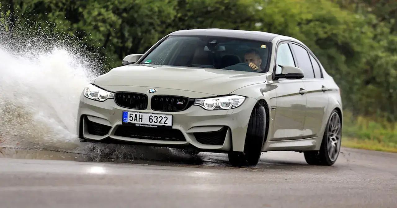 Szary BMW F80 M3 pokonuje kałużę, tworząc efektowny rozbryzg wody.