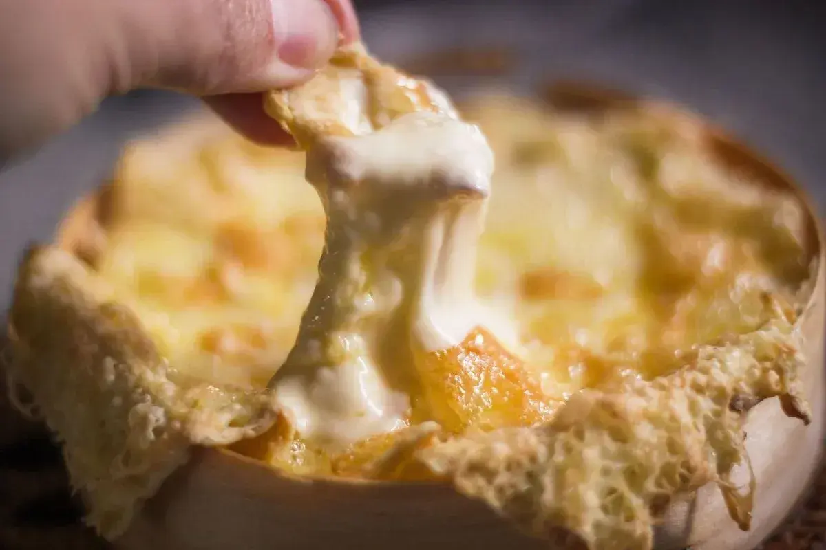 Un morceau de pain trempé dans un fromage fondu doré, prêt à être dégusté. Une invitation à découvrir la recette du Berthoud.