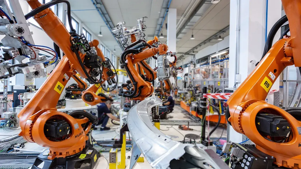 Pomarańczowe ramiona robotów KUKA pracują w fabryce, tworząc przyszłość. To zaawansowana robota automatyka.