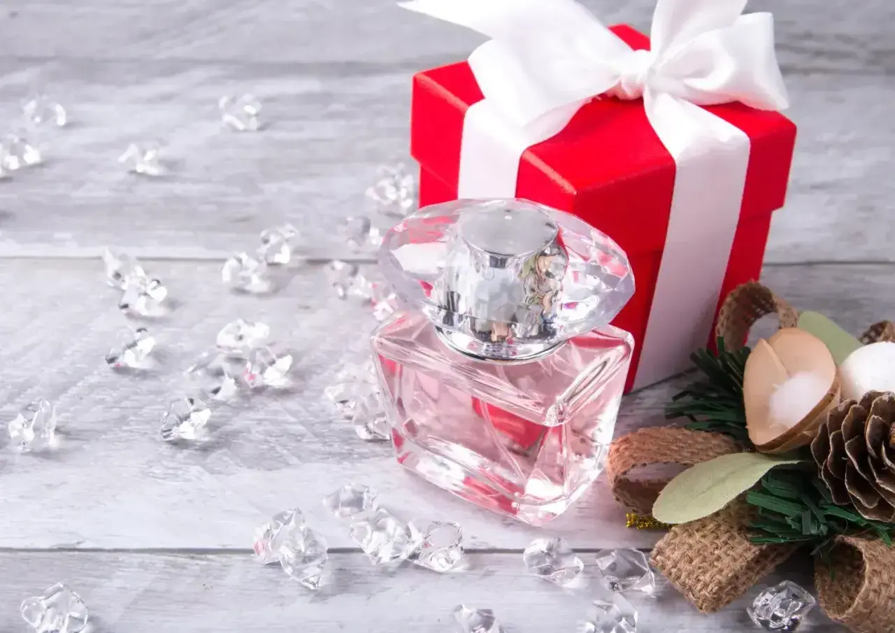Eleganckie perfumy w szklanej butelce, czerwone pudełko z kokardą i ozdoby. Idealny pomysł, jak zapakować perfumy na prezent.