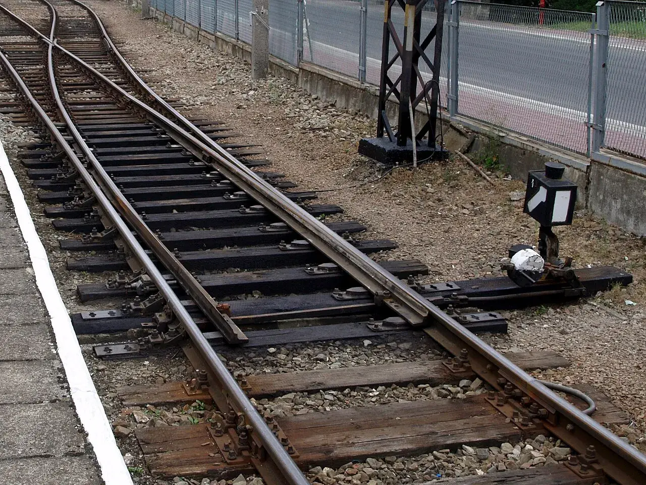 Zwrotnica kolejowa z nastawczym suwakowym mechanizmem. Minimalna droga oporowa klamry w zamknięciu nastawczym suwakowym jest kluczowa dla bezpieczeństwa.