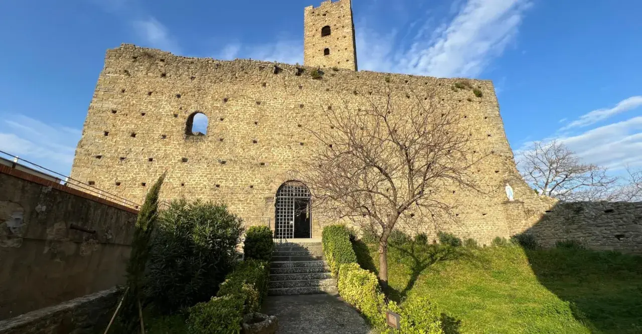 Rovine del castello di Larciano Pistoia, con torre, mura in pietra e un piccolo giardino curato.