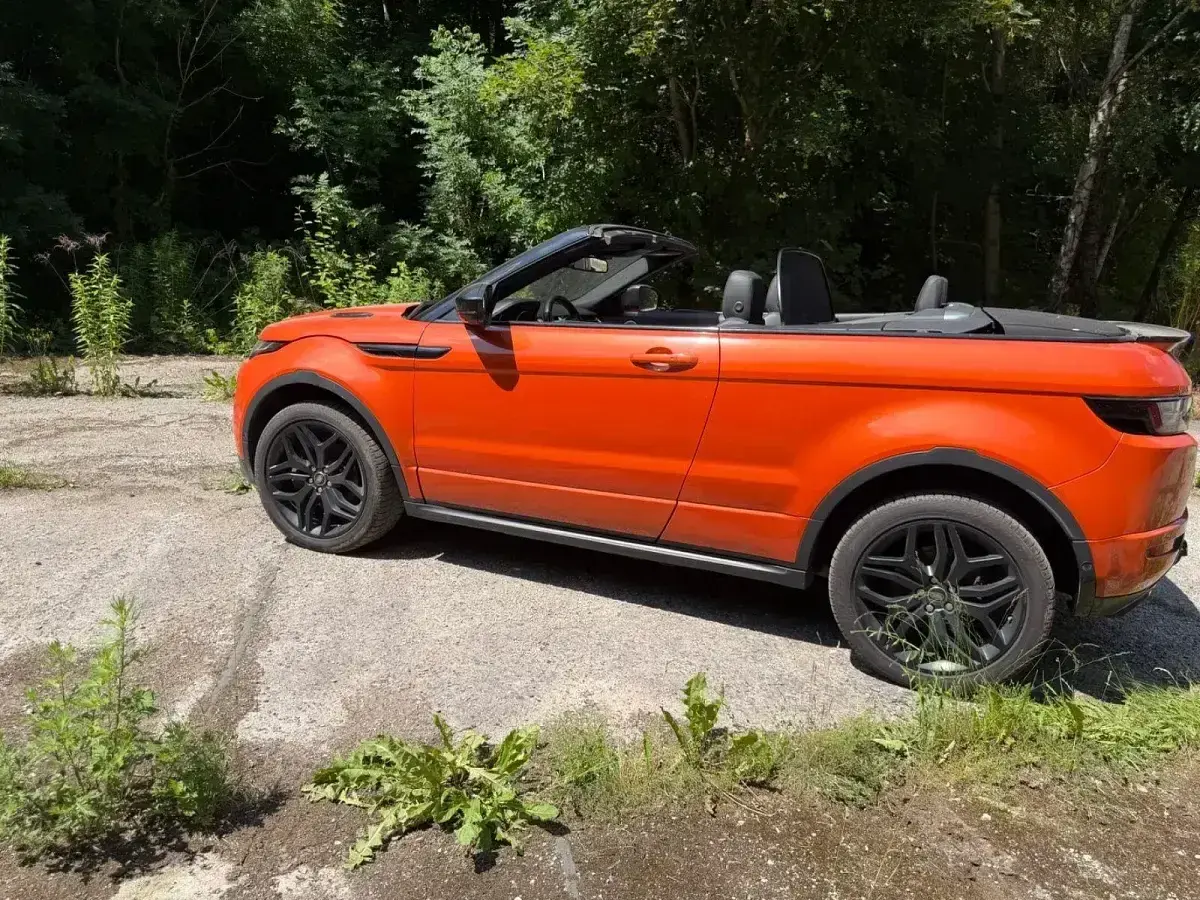 Orange Range Rover Evoque Cabrio, offen, steht auf einem Schotterweg. Mögliche Probleme mit dem Verdeck?