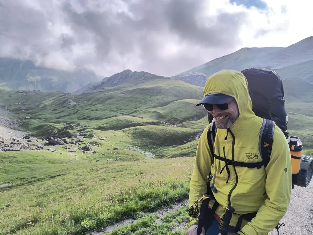Uśmiechnięty turysta w żółtej kurtce z plecakiem podziwia malownicze góry Rumunii.