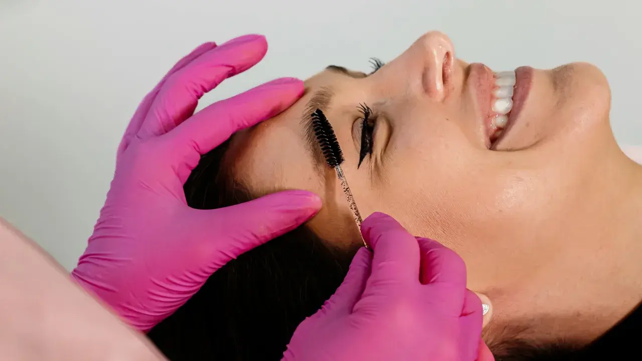 Manos con guantes rosas peinan cejas. Es parte de que es el laminado de cejas, un tratamiento para dar forma y fijar el vello.