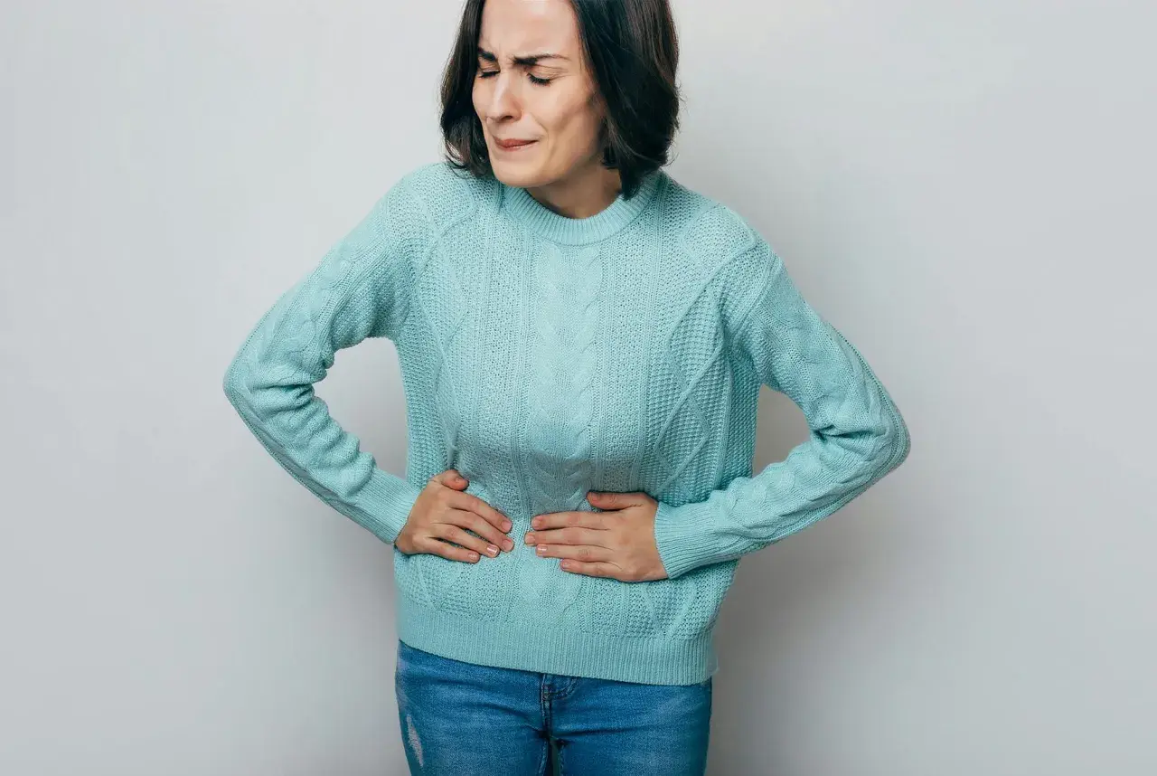 Kvinna med händerna på magen, ansiktet förvridet av smärta. Ett tydligt tecken på stressmage symptom.