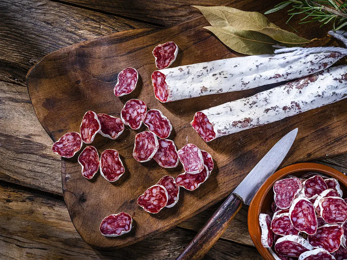 Tranches de saucisson sec, entiers et coupés, sur une planche en bois. On peut cuire du saucisson sec pour le déguster chaud.