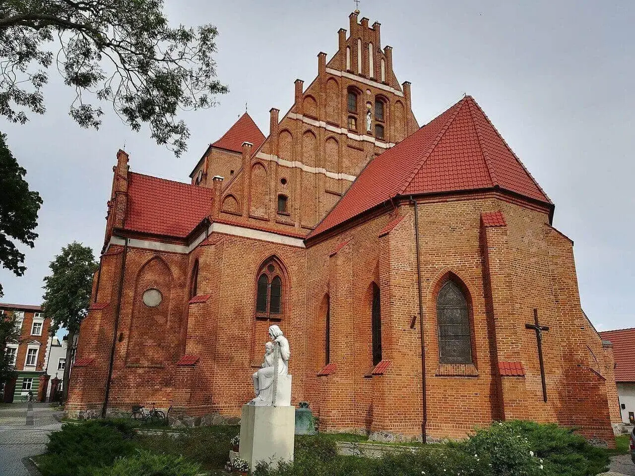 Majestatyczny kościół w Pucku z cegły, z czerwonym dachem i rzeźbą Matki Boskiej.