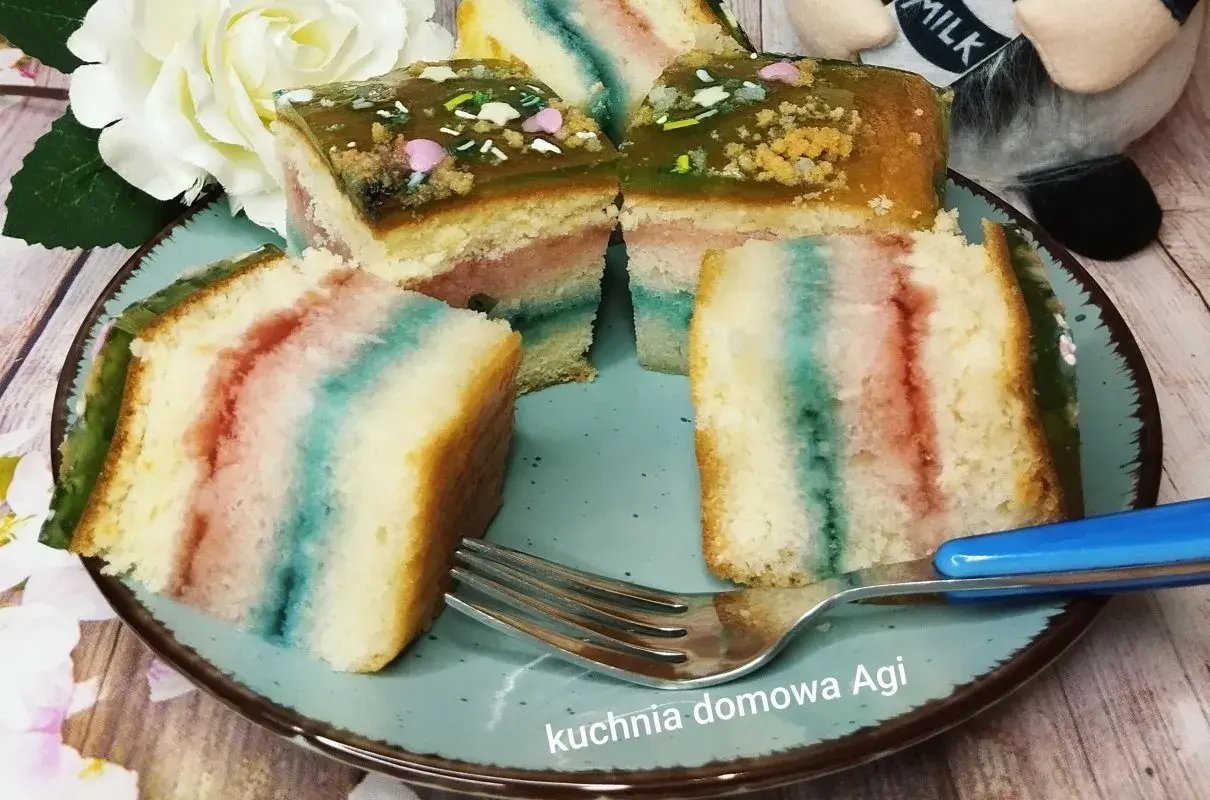 Kolorowy biszkopt z galaretką i posypką na talerzu, obok widelec.