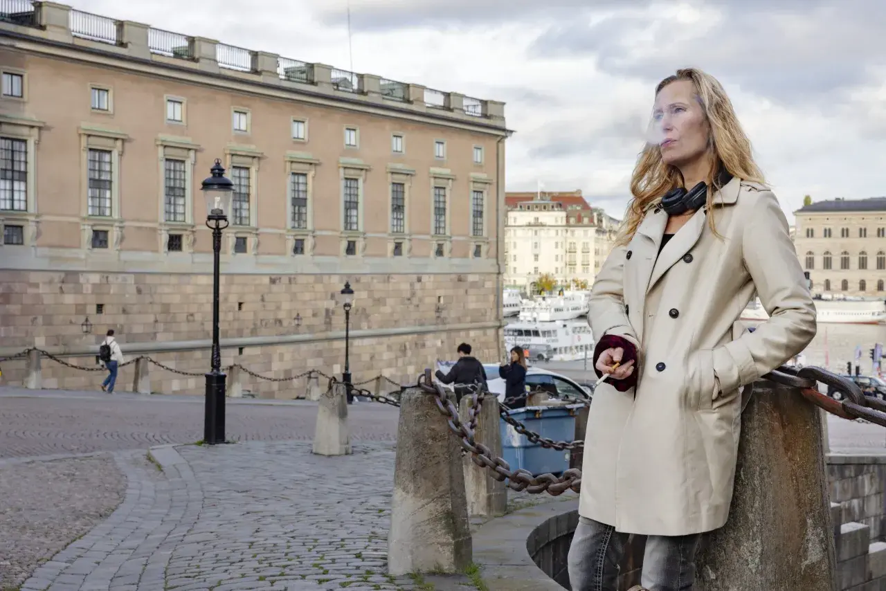 Sara Mac Key, med hörlurar runt halsen, tar en cigarettpaus vid vattnet i Stockholm.