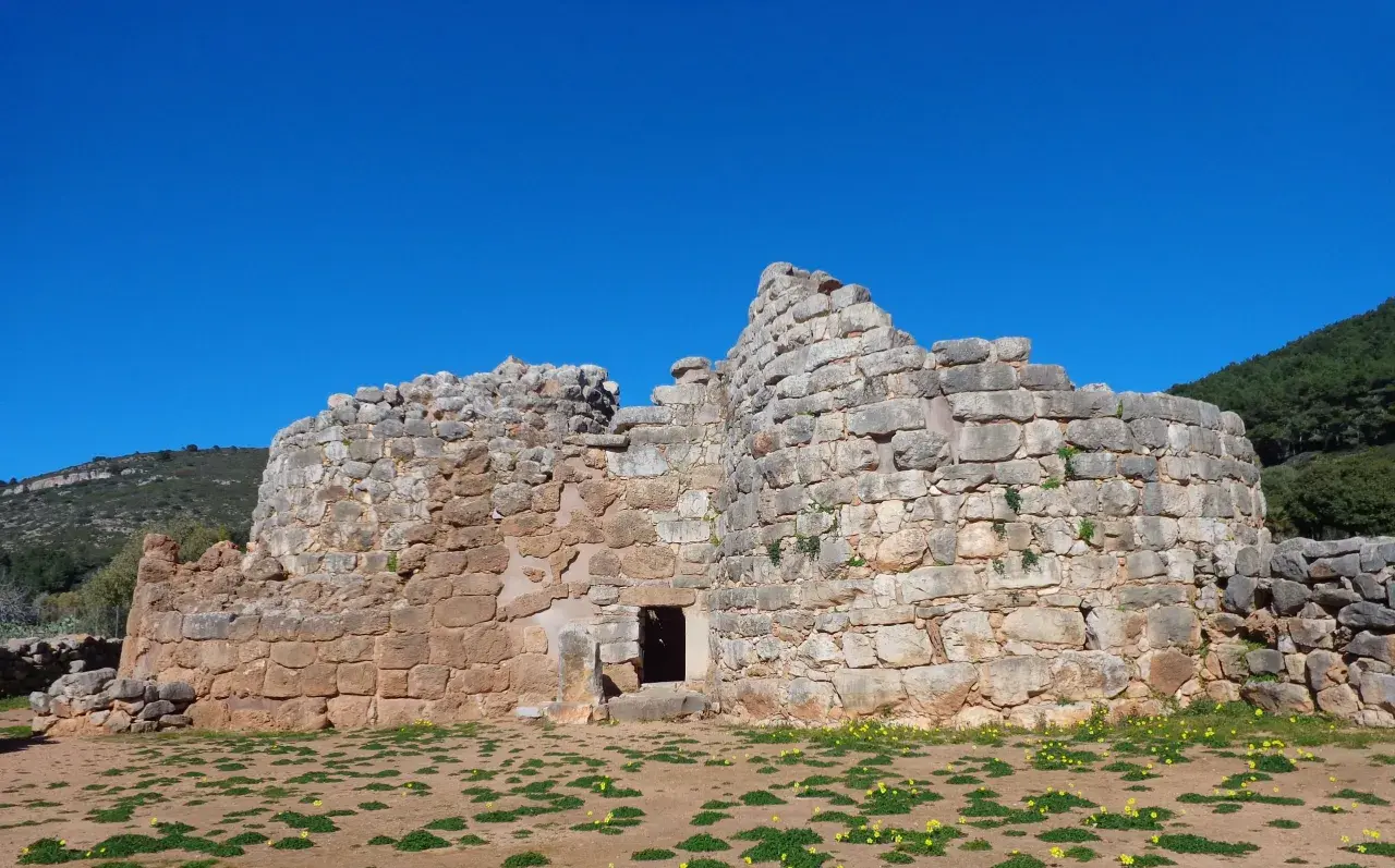 Il nuraghe Palmavera, imponente struttura in pietra sotto un cielo azzurro, testimone di antiche civiltà.