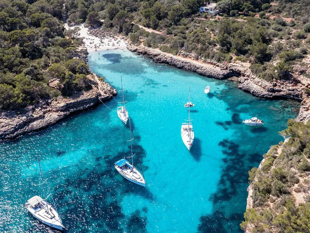 Traumhafte Bucht mit türkisfarbenem Wasser, Segelbooten und einem Strand – ein echter Mallorca Geheimtipp für unvergessliche Urlaubstage.