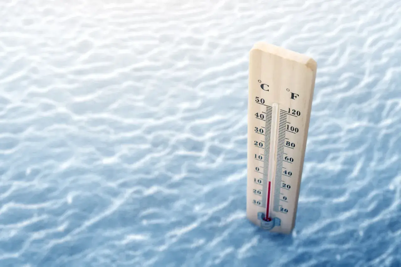 Drewniany termometr pokazuje, że ile stopni ma Bałtyk w sierpniu, wskazując ok. 20°C. Woda jest lekko falująca.