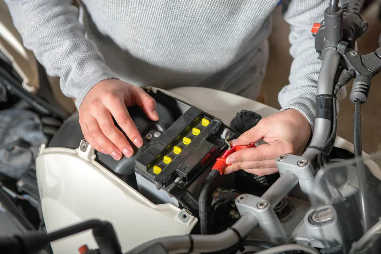 Ręce podłączają kable do akumulatora motocyklowego, szukając odpowiedzi, dlaczego akumulator się rozładowuje.