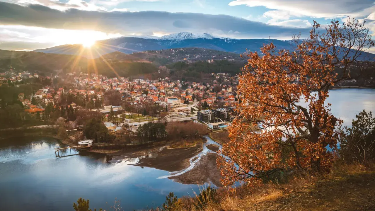 Widok na miasteczko nad jeziorem, góry w tle. Idealne miejsce, gdzie na wakacje w sierpniu, choć liście drzew już brązowe.