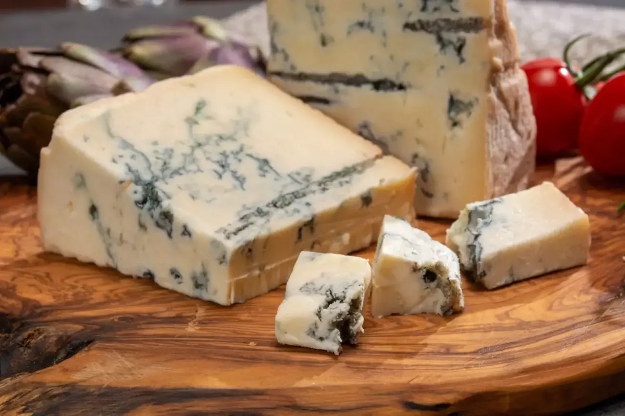 Pezzi di gorgonzola su tagliere di legno, con carciofi e pomodorini. Un assaggio dell'autentica gorgonzola origine.