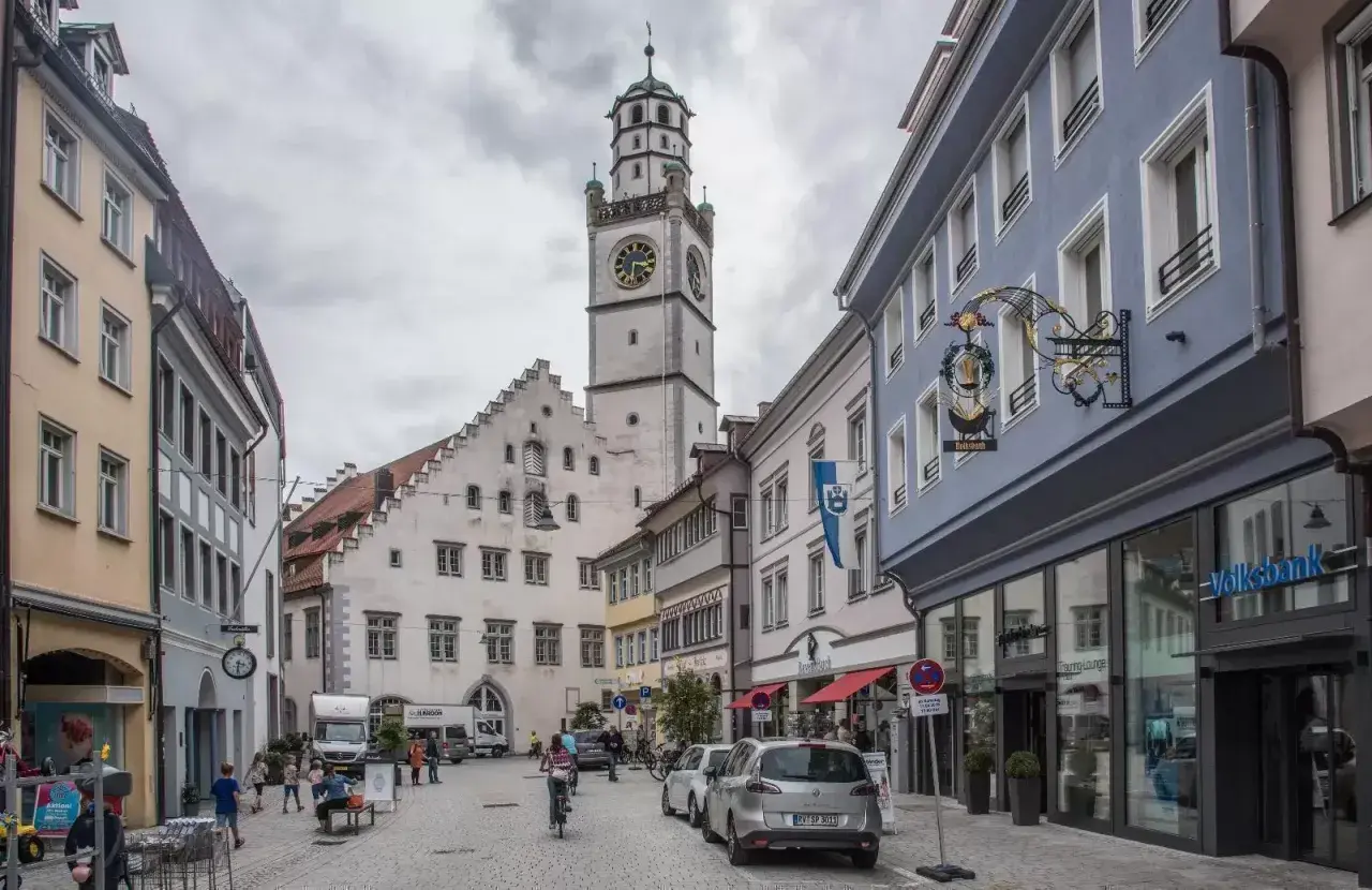Der Blaserturm Ravensburg ragt über eine belebte Gasse mit Geschäften und Menschen.
