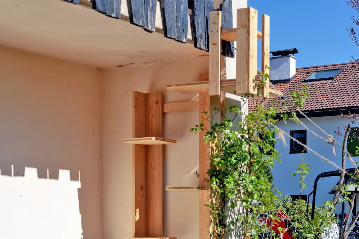 Selbstgebaute katzentreppe aus Holz, die an einer Hauswand befestigt ist. Mehrere Ebenen laden zum Klettern ein.