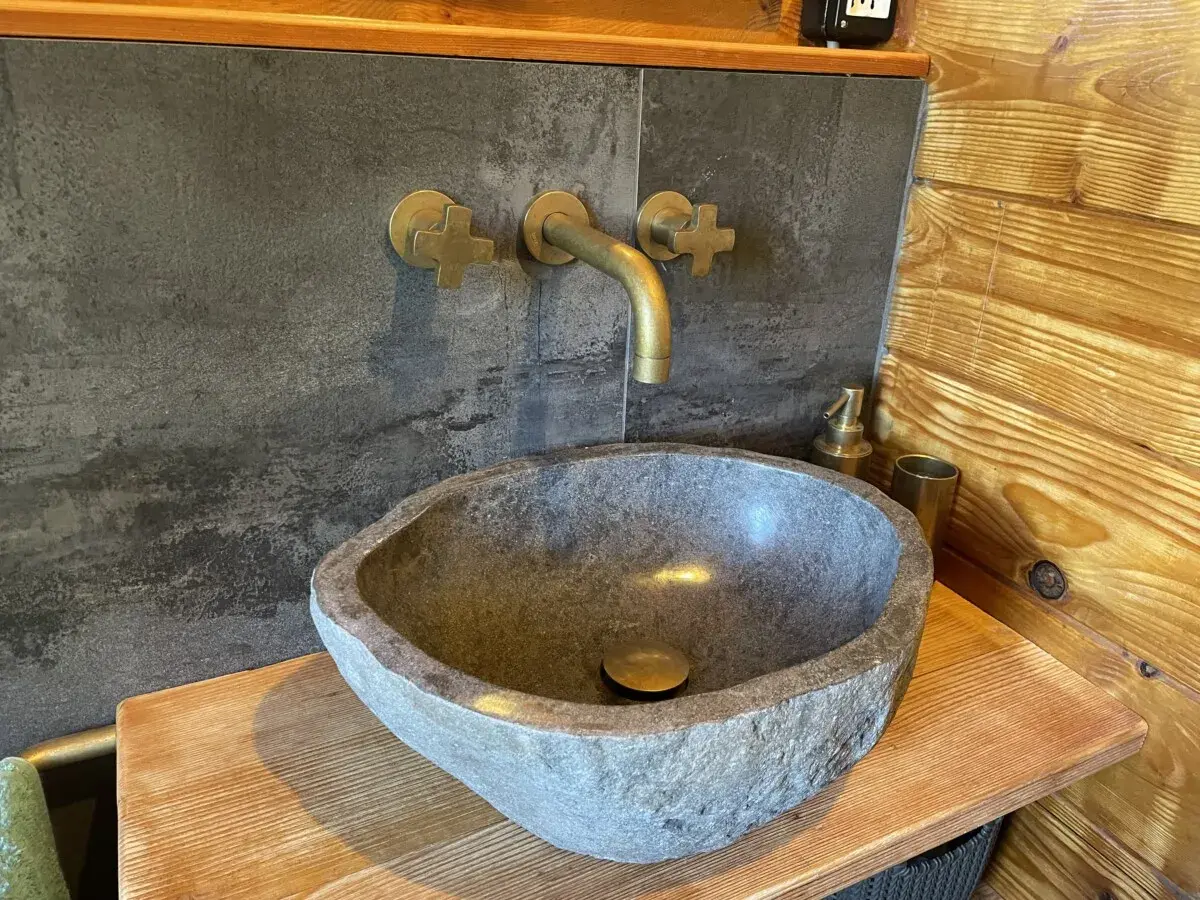 Lavabo in pietra grezza, rubinetteria in ottone e rivestimento in legno: perfette idee bagno montagna per un'atmosfera rustica e accogliente.